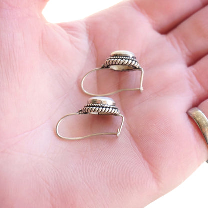 Vintage silver moonstone drop earrings sitting on open palm, featuring ornate banded design and secure kidney ear wire closures.