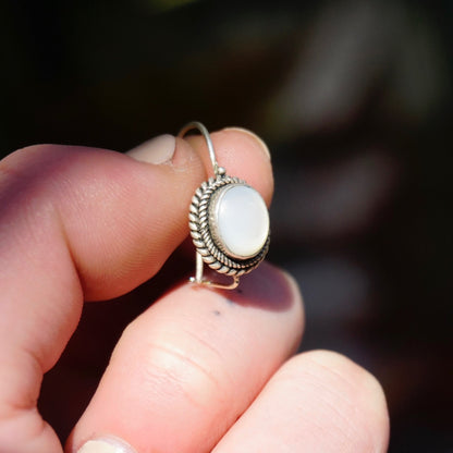 Vintage silver moonstone drop earrings with petite locking hook kidney ear wires, held in fingers to show detail of the delicate silver setting surrounding the round white moonstone cabochons.