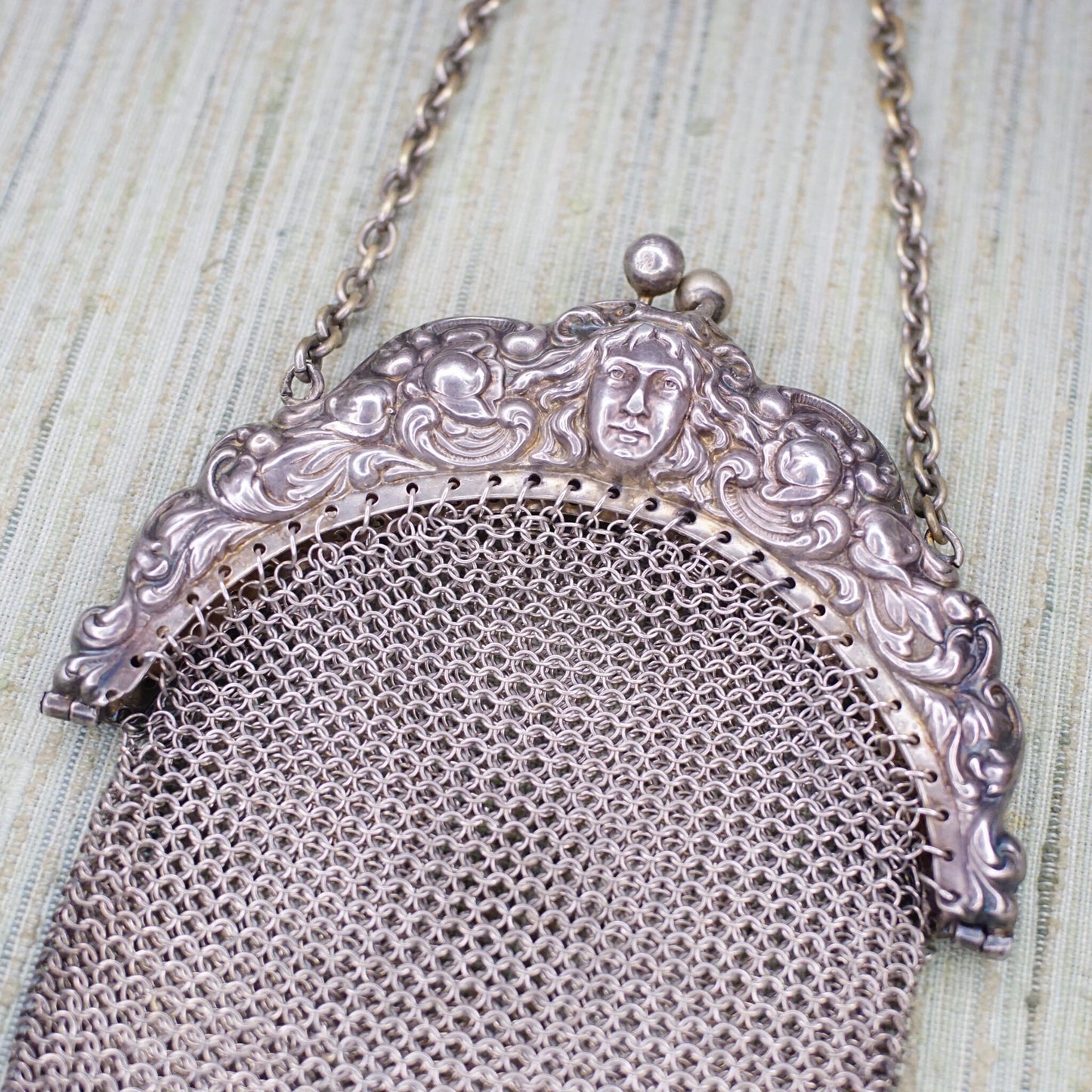 Antique Art Nouveau sterling silver chain mail mesh coin purse with embossed decorative face design on the frame, in excellent vintage condition.