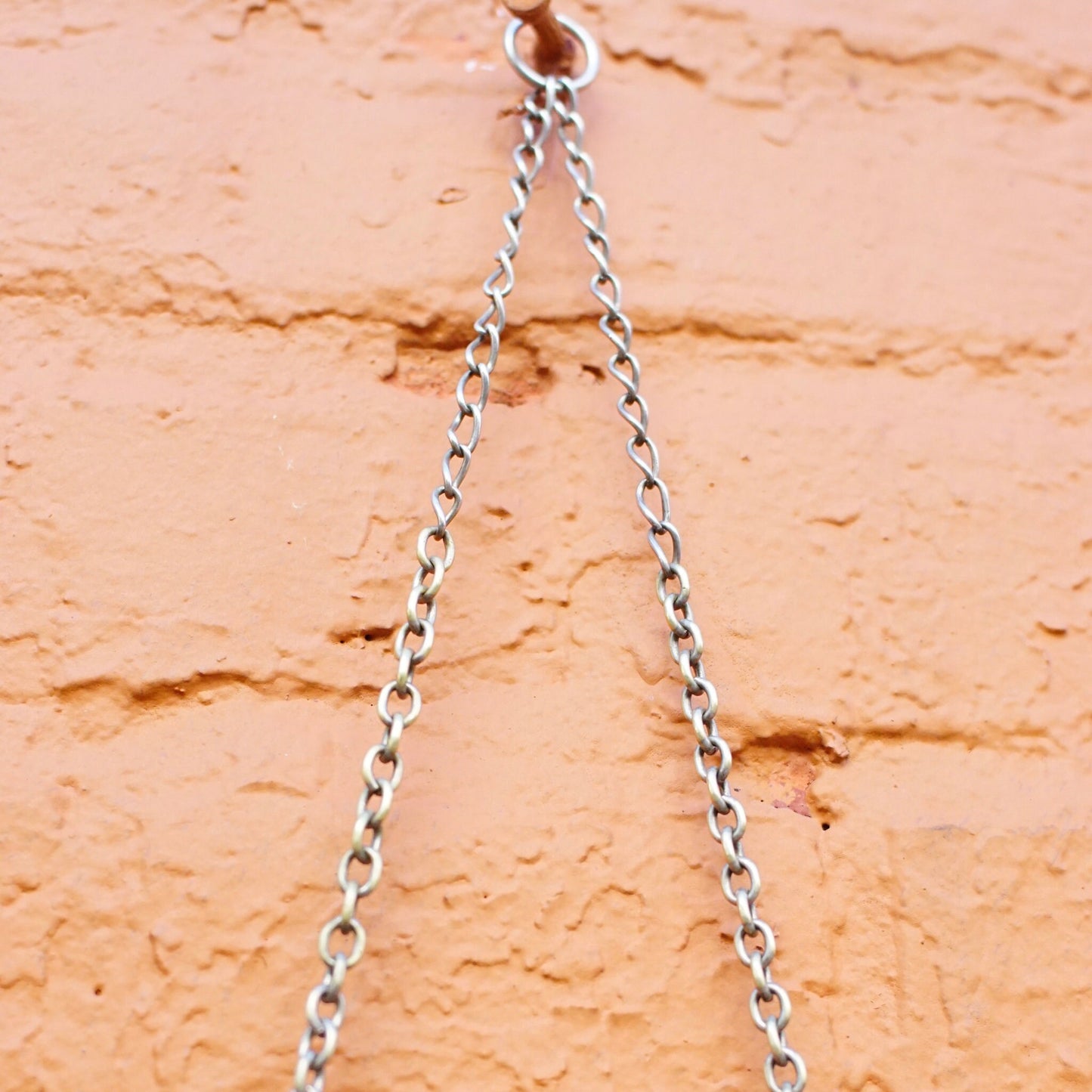 Antique Art Nouveau sterling silver chain mail purse with embossed face on frame, hanging against an adobe brick wall. The purse is in vintage condition with an intricate silver mesh design and a 925 sterling silver mark.