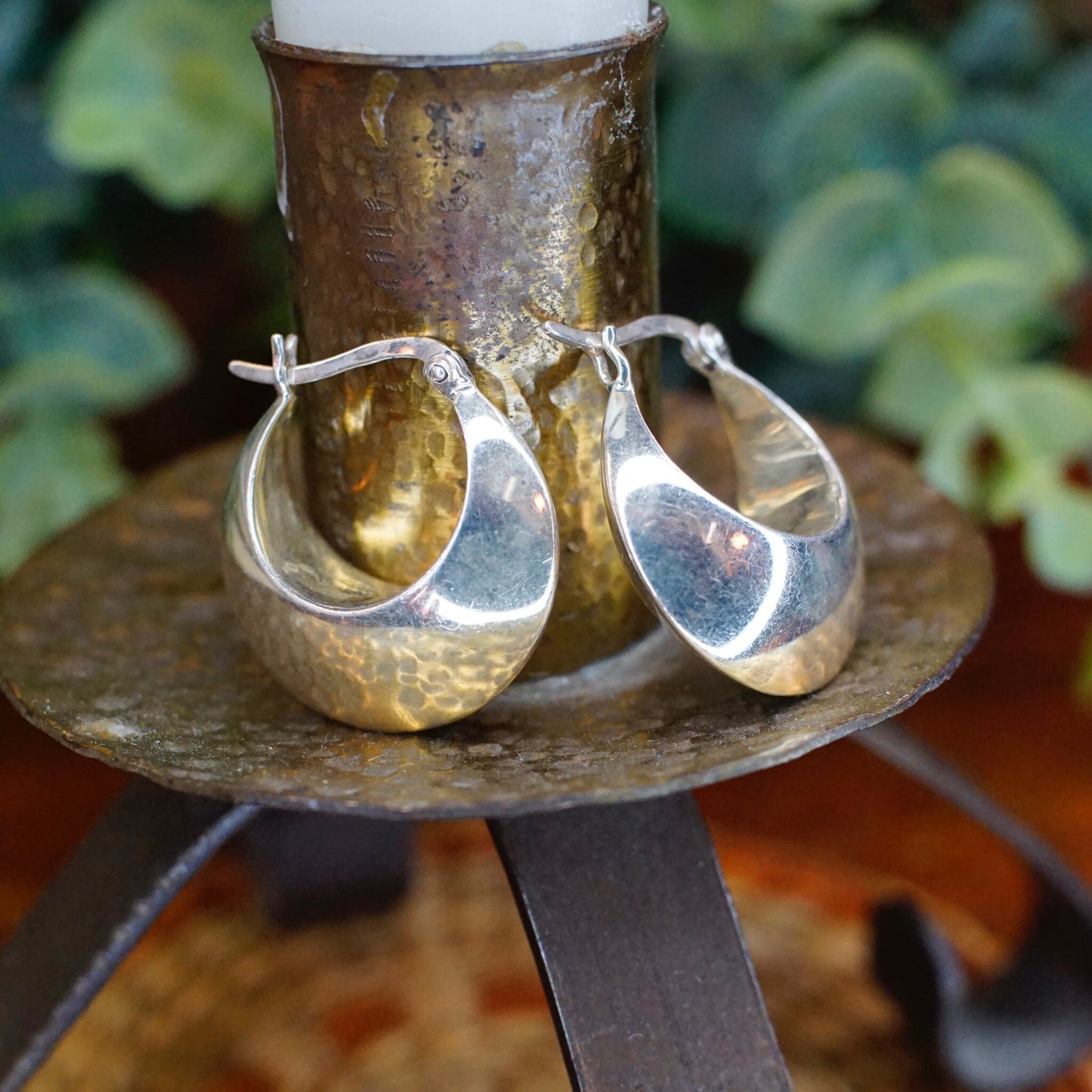 Vintage sterling silver half moon hoop earrings against rustic wooden stand and blurred greenery background