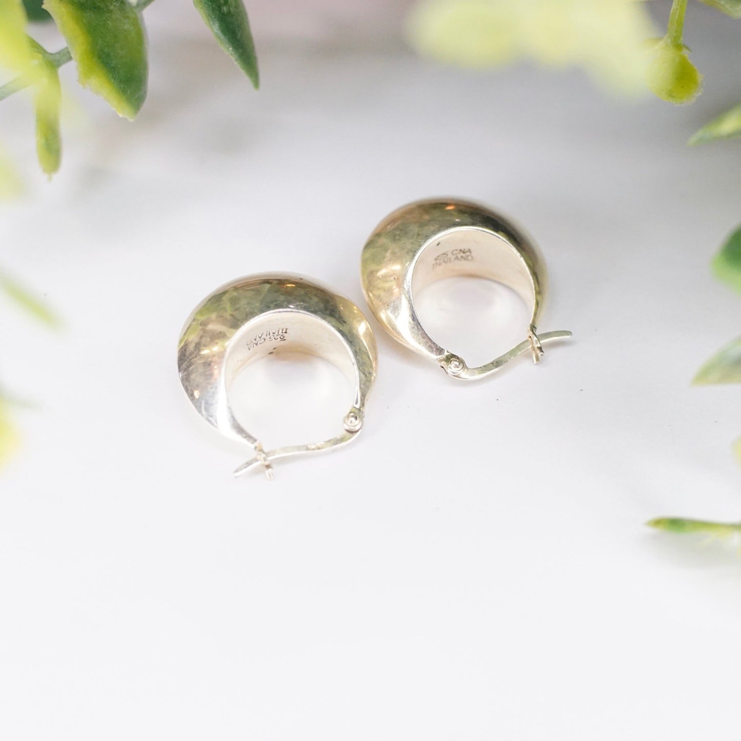 Vintage sterling silver half moon hoop earrings on white background with green leaves