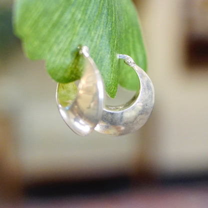 A water droplet hangs from the tip of a green leaf, reflecting the surroundings in its clear, rounded surface.