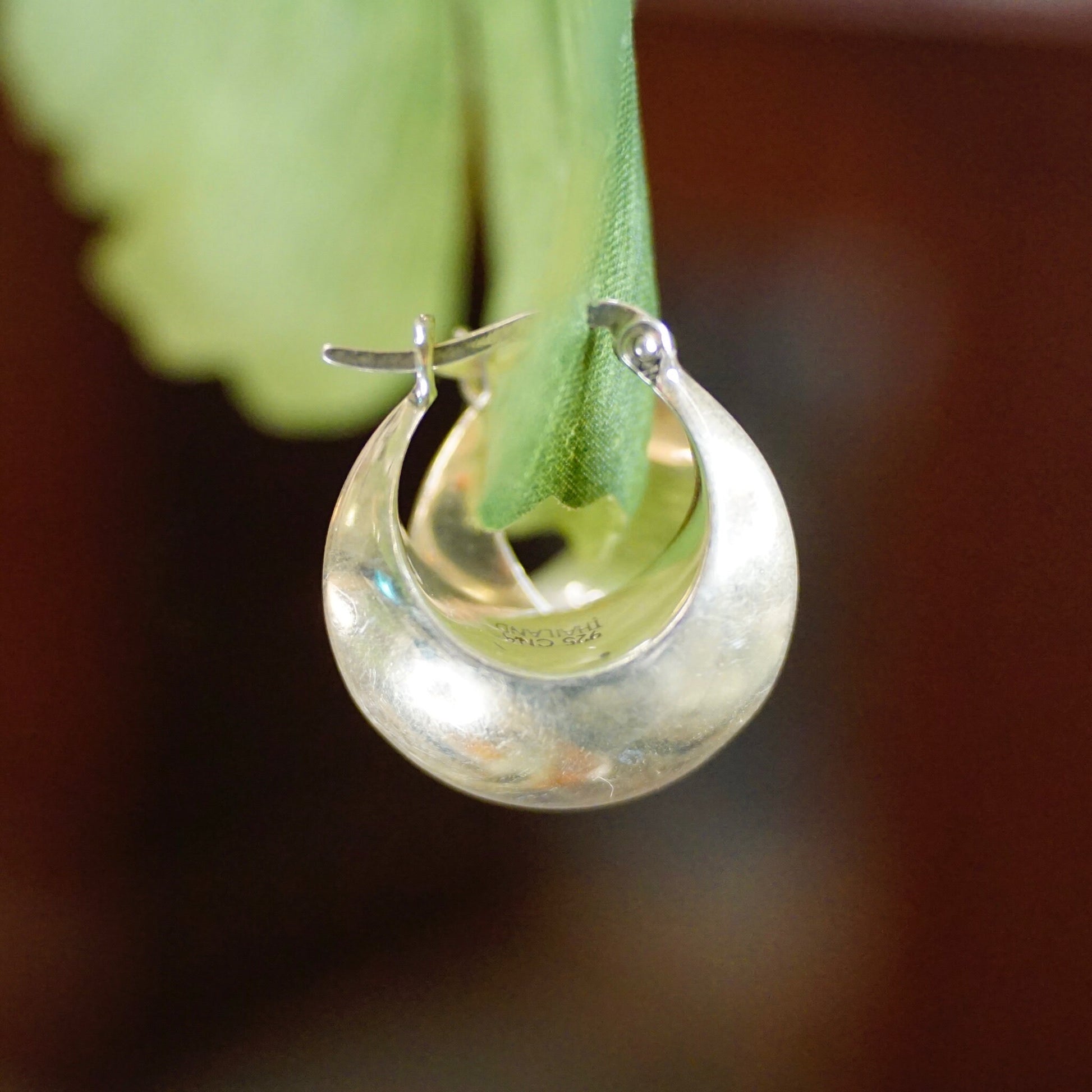 Sterling silver half moon hoop earrings with green peridot gemstones hanging from leaf on closeup of flower petal