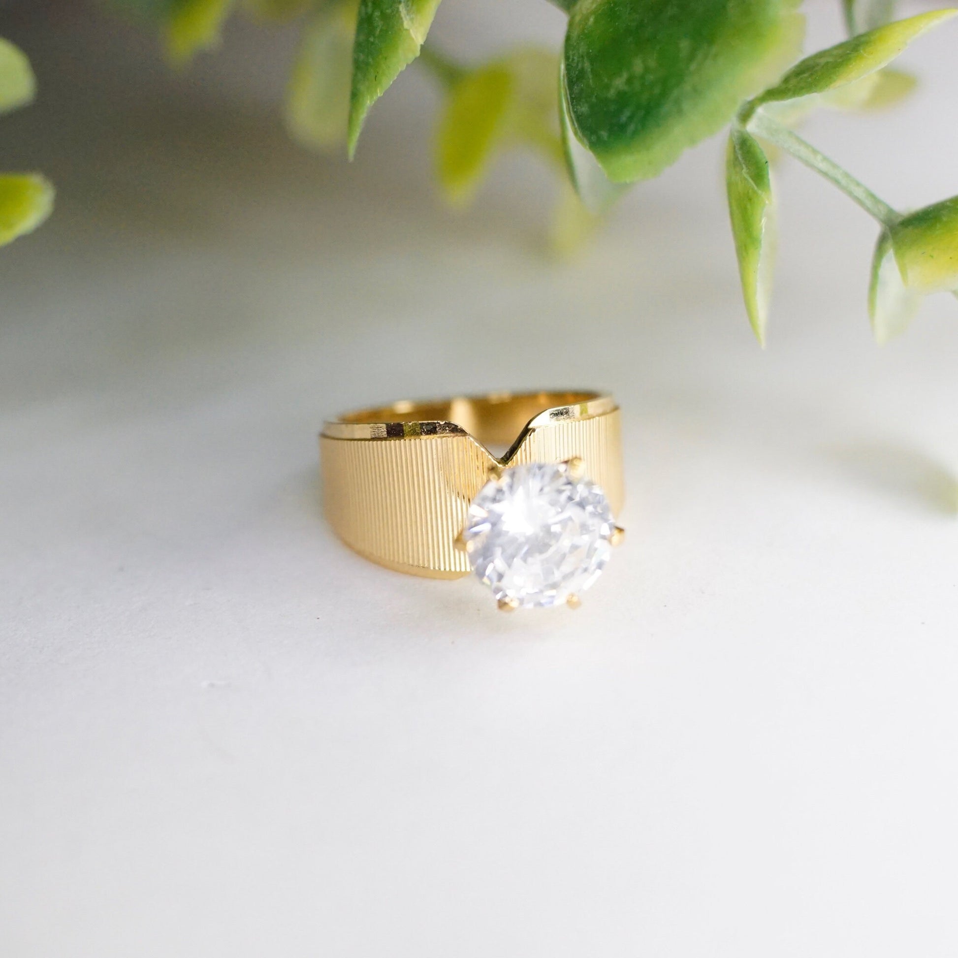 Vintage gold tone solitaire ring with round cut cubic zirconia stone on a background of green leaves