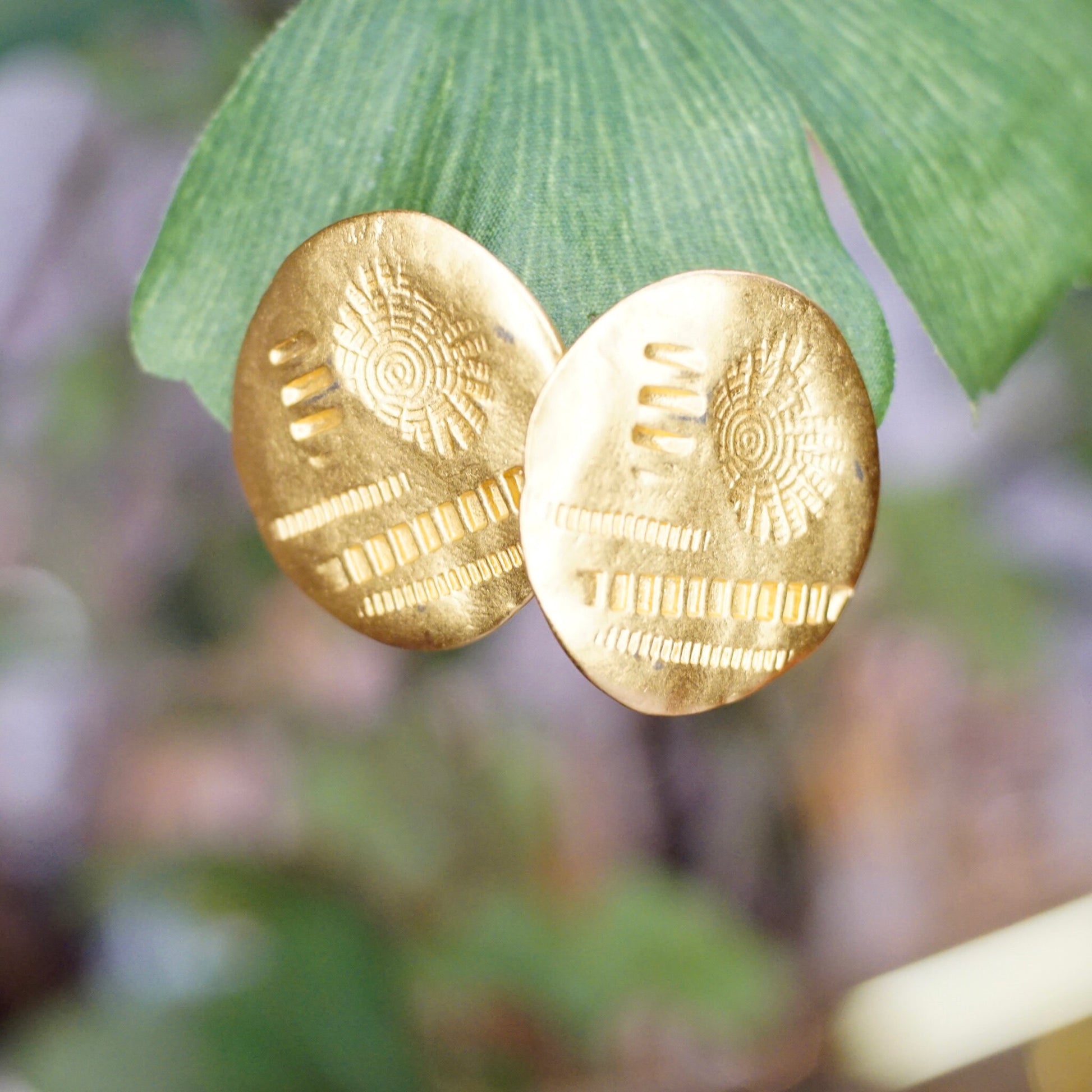 Vintage gold tone hammered disc stud earrings with abstract stamped details, shown on green leaves