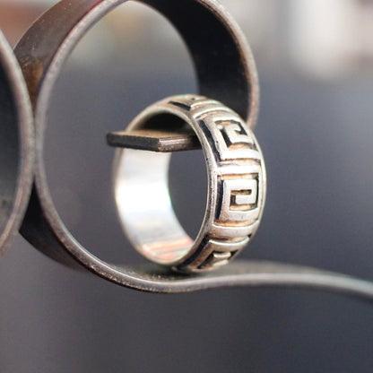 Vintage sterling silver square swirl ring with thick Greek key band design, a solid dome shape, and 925 purity stamp, shown in close-up against a blurred background. The ring is a US size 9 3/4.