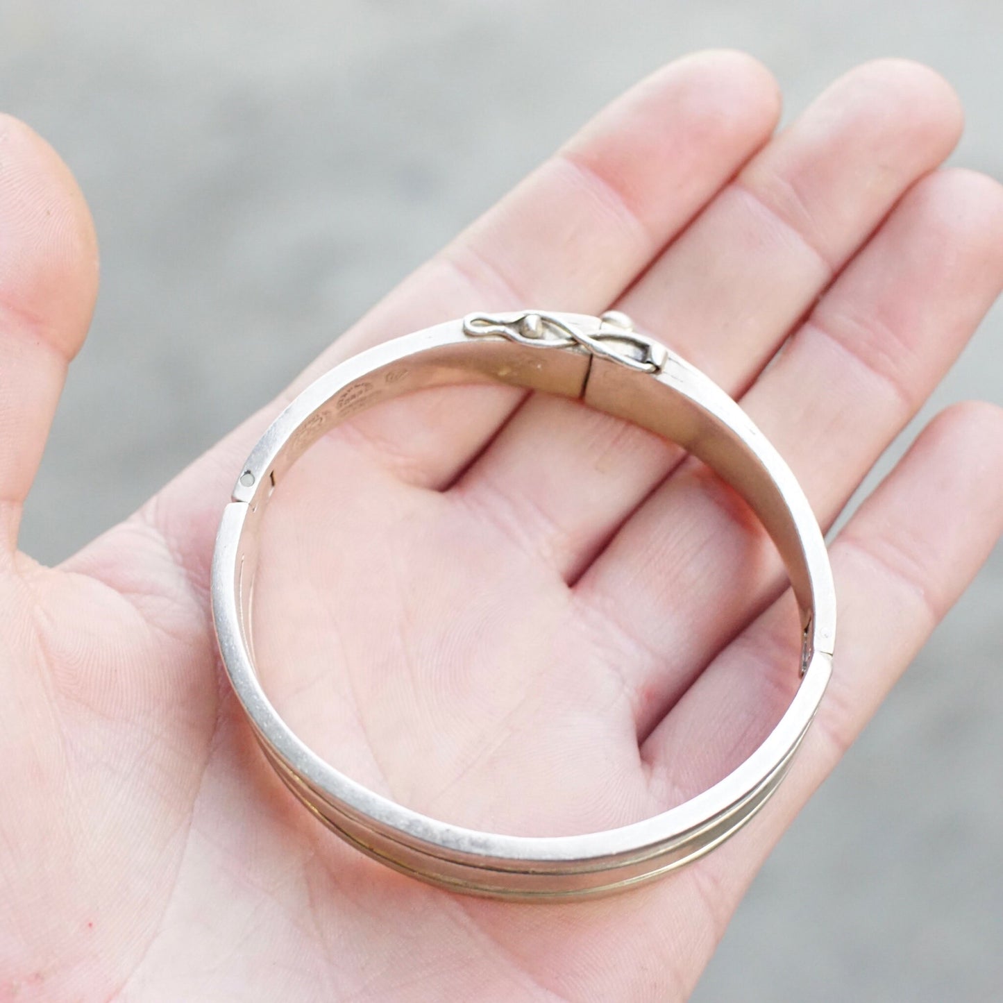 Vintage sterling silver hinged bangle bracelet with cut out design from Taxco, Mexico, measuring 6 1/2 inches long, held in a person's palm