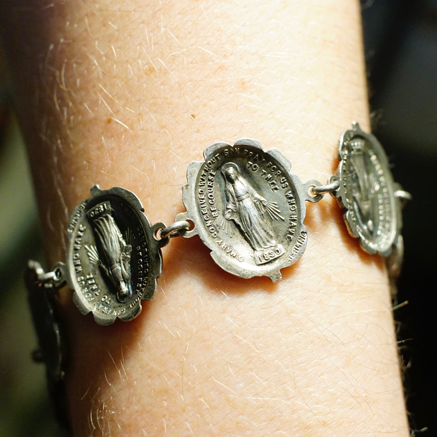 Vintage HMH sterling silver rosebud and Mother Mary reversible link bracelet, featuring circular charms with religious iconography on both sides, attached to a silver chain on a person's wrist.