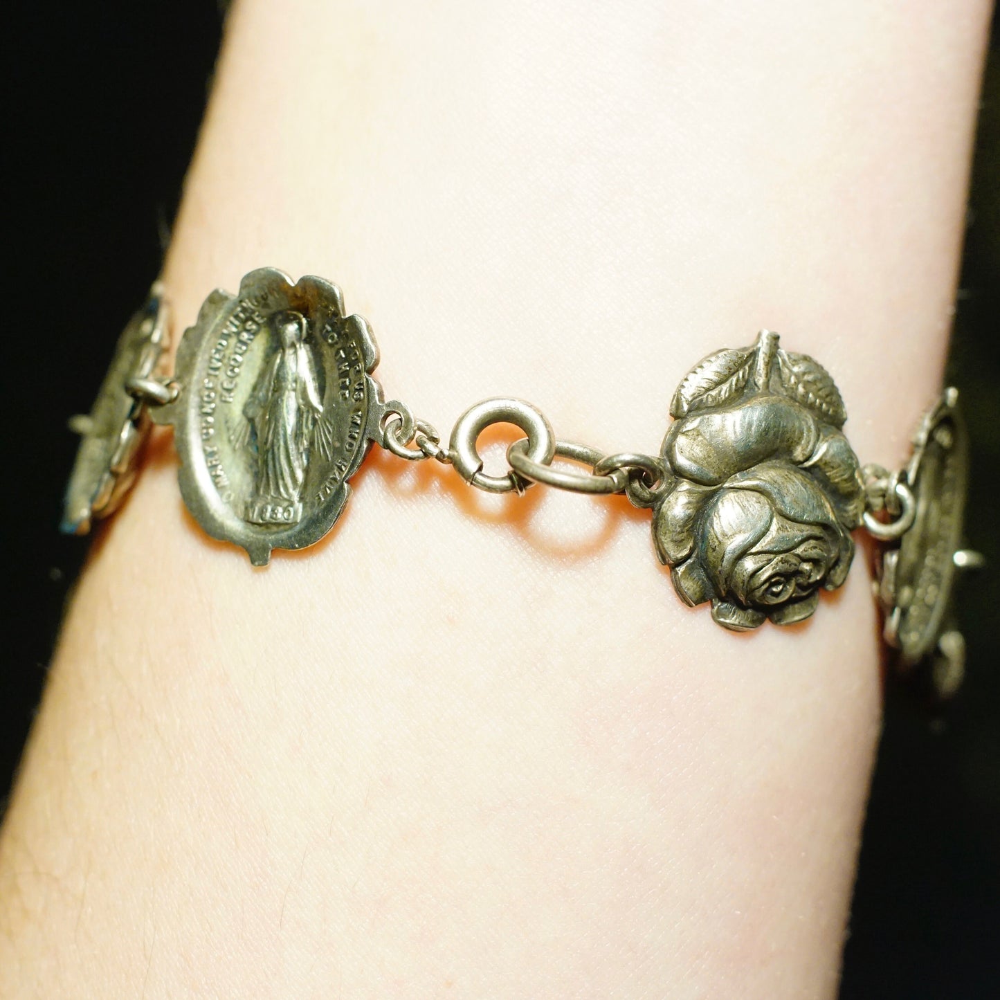 Vintage sterling silver bracelet with reversible charms featuring a rosebud and the Virgin Mary, a religious jewelry piece with intricate floral and saint designs.