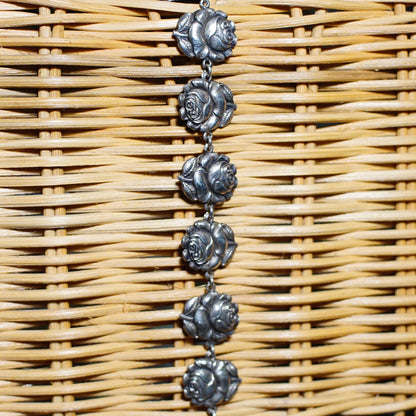 Sterling silver rosebud and Mother Mary charm bracelet on woven rattan background