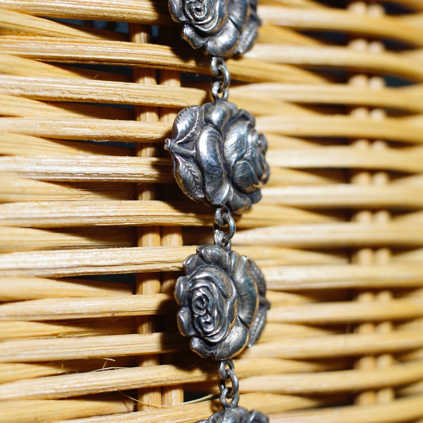 A close-up of a vintage sterling silver bracelet featuring rose-shaped links on one side and reversible charms depicting the Virgin Mary on the other, laid on a woven wooden surface.