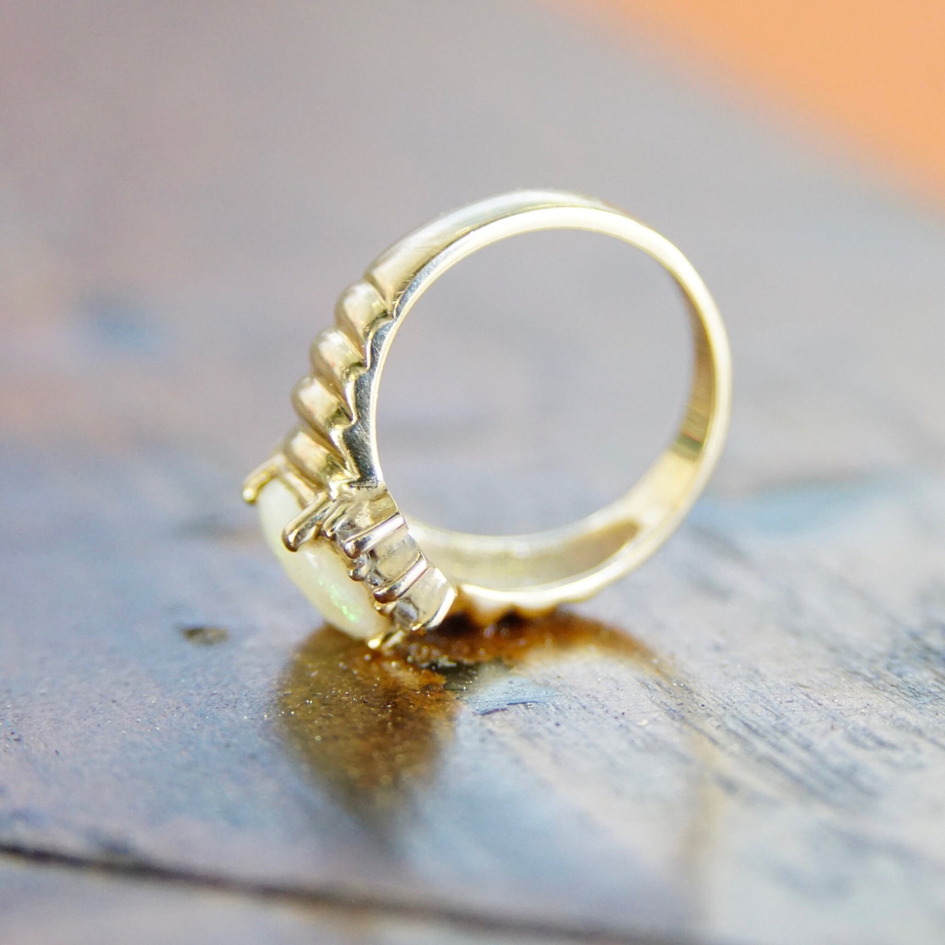 Vintage 14K yellow gold ring featuring an oval opal center stone accented by small diamonds in a graduated design, displayed on a weathered blue wooden surface.