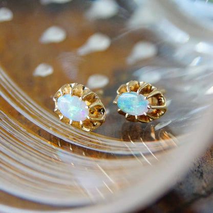 Vintage 14K gold opal stud earrings with prong setting and opalescent glow on textured gold surface, petite size, October birthstone jewelry