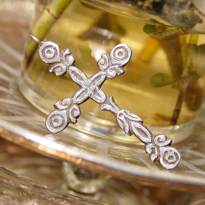 Ornate sterling silver gothic cross pendant with hammered texture and oxidized silver design, displayed on a reflective gold surface.