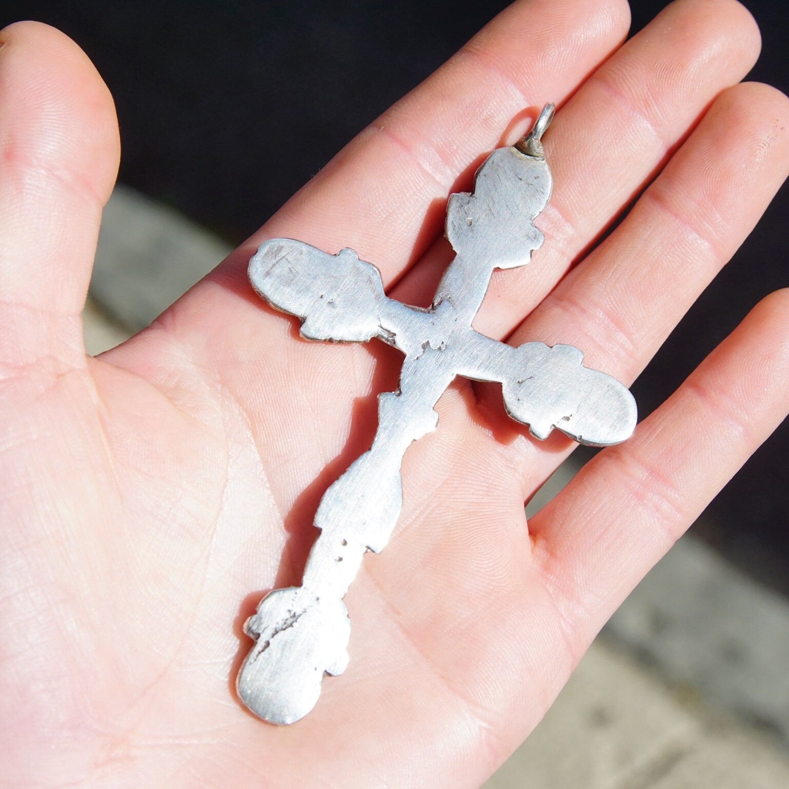 Large silver cross pendant resting in an open hand, showing intricate oxidized hammered silver design against the skin.