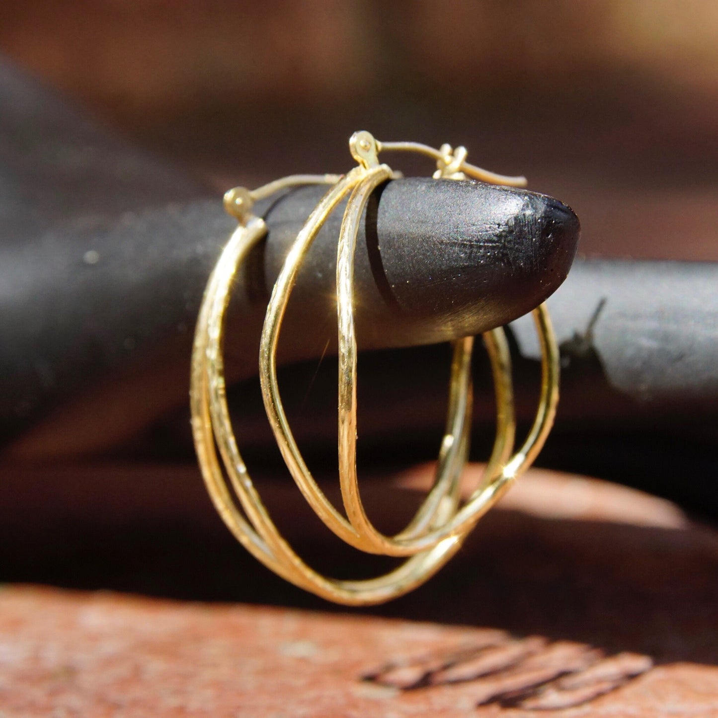 Vintage 14K gold hammered double strand hoop earrings with textured oval design and hinged clasp on wooden surface.