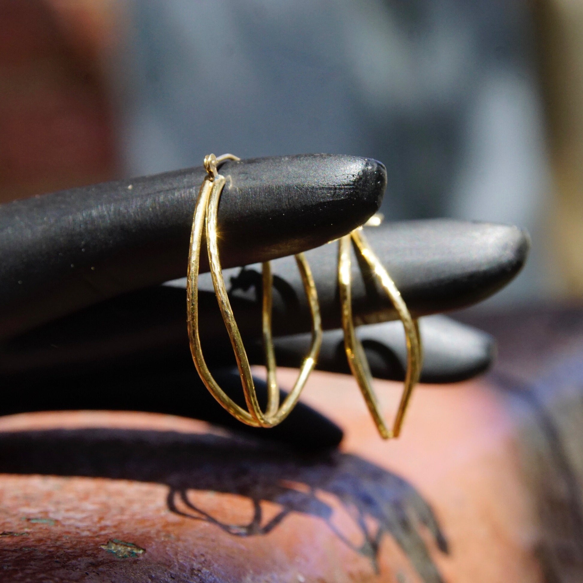 Vintage 14K gold hammered double hoop earrings with textured oval design and hinged clasp, resting on wood surface.