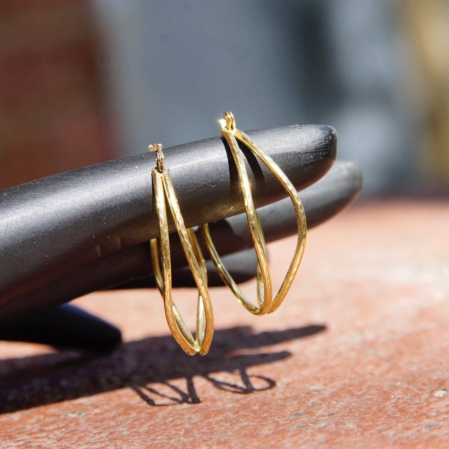 Close up view of two gold hoop earrings resting on a rust-colored textured surface, showing the hammered texture and hinged clasp design of the oval-shaped vintage 14K gold earrings.