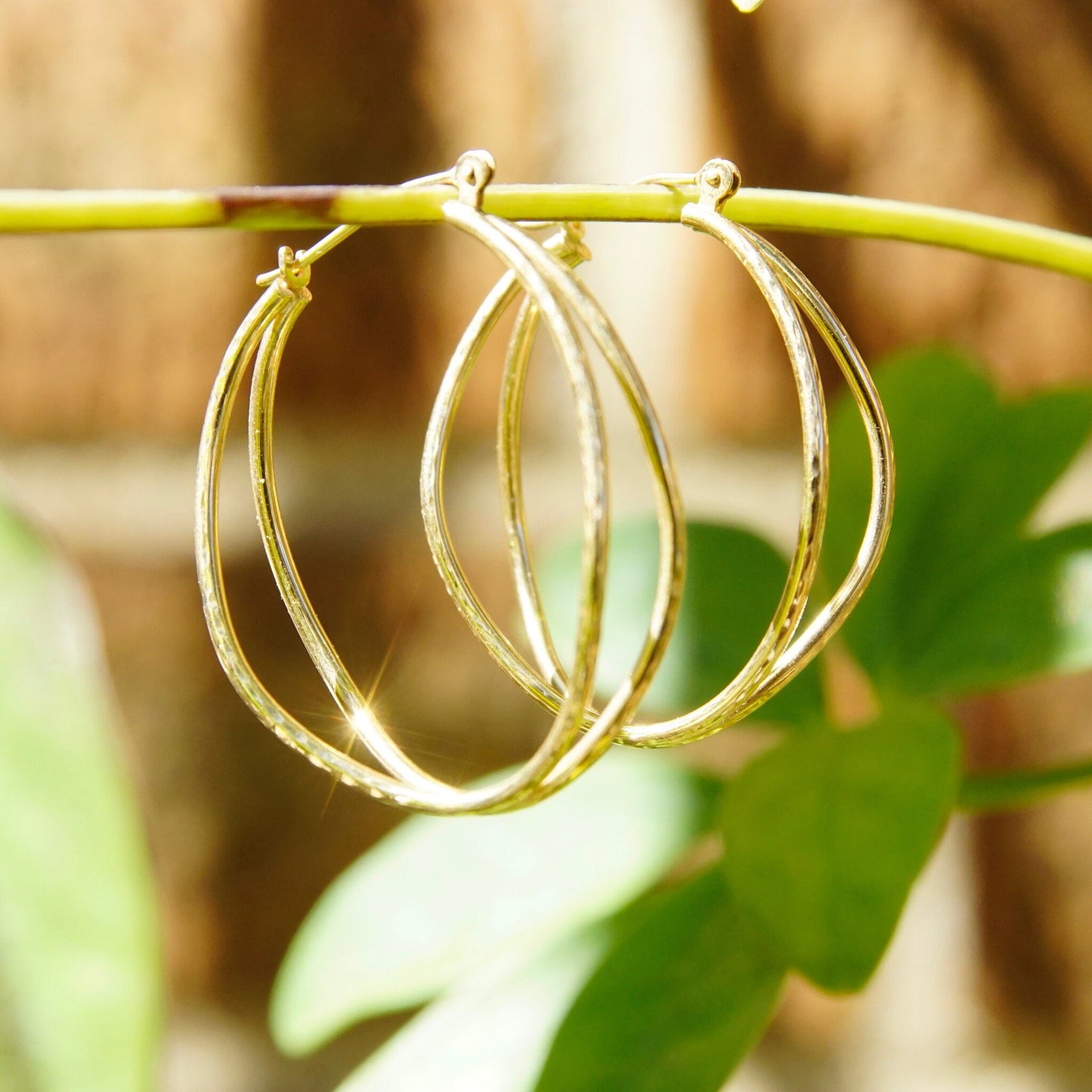 Vintage 14K gold hammered double strand hoop earrings hanging from green leaf, textured oval hoops with hinged clasp, minimalist wire design, 1 1/4 inches long.