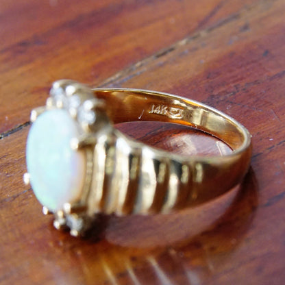 Vintage 14K yellow gold cocktail ring featuring a beautiful center opal stone accented by graduated diamonds, size 6 1/4 US, displayed on a wooden surface.