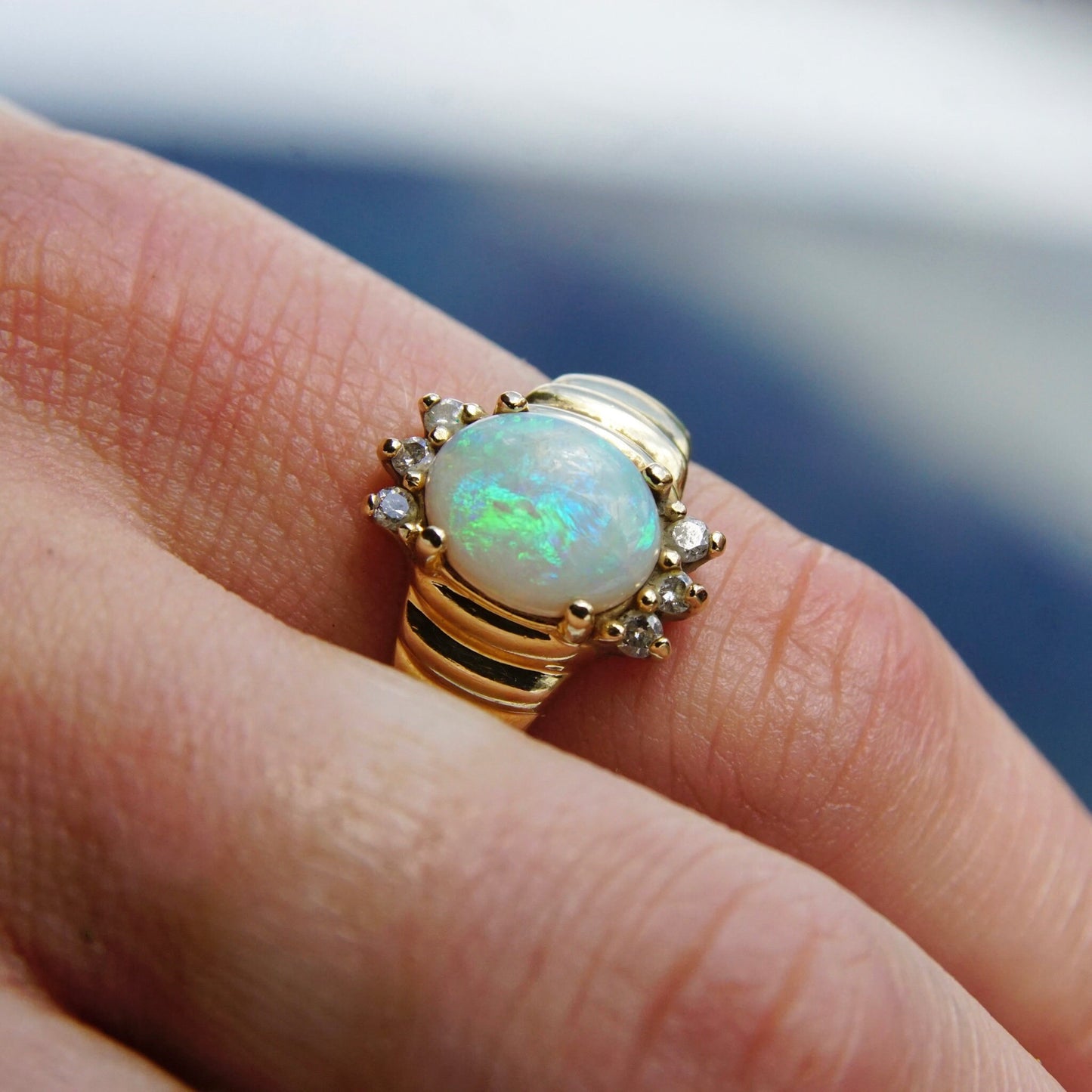 Vintage 14K yellow gold opal and diamond cocktail ring featuring a beautiful oval opal cabochon center stone accented by small diamonds, shown on a finger.