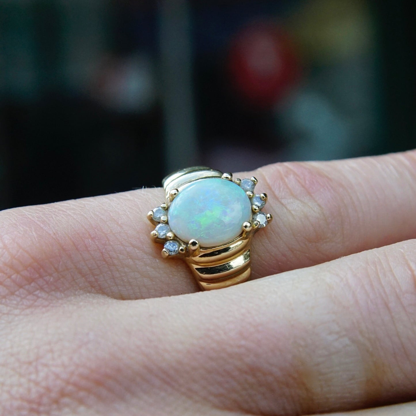 Vintage 14K gold opal and diamond cocktail ring on finger, featuring a beautiful oval opal center stone surrounded by small accent diamonds, set in a graduated 14K yellow gold band, ring size 6 1/4 US.