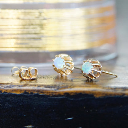 Vintage 14K gold prong set opal stud earrings with opalescent stones and gold backings on rustic wooden surface