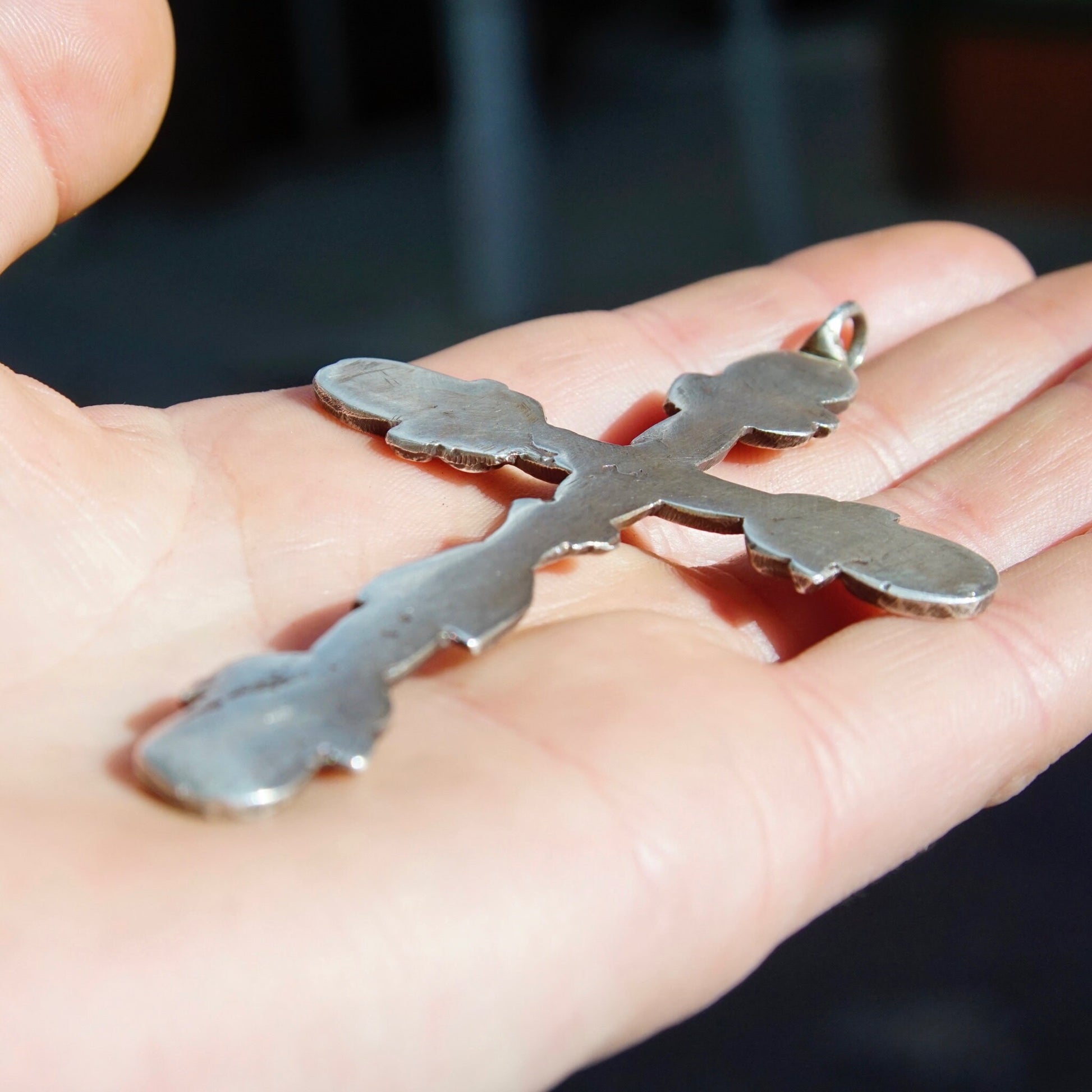 Vintage large sterling silver gothic cross pendant resting on an open hand, showing intricate hammered detailing and oxidized silver design. The ornate cross measures approximately 4 inches long.