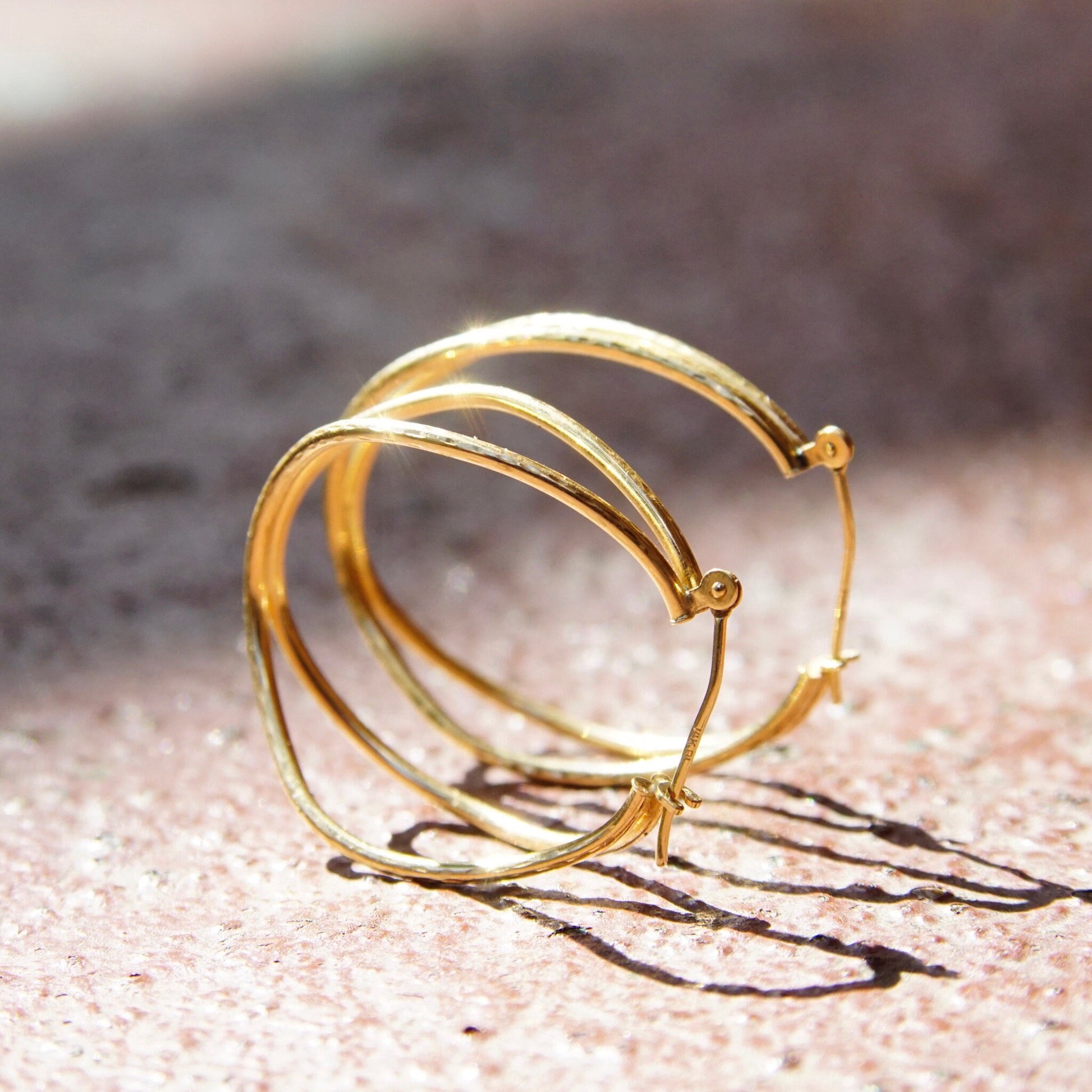 Vintage 14K gold hammered double strand hoop earrings with textured oval design and hinged clasp, minimalist gold wire hoops measuring 1 1/4 inches long, on grungy textured surface.