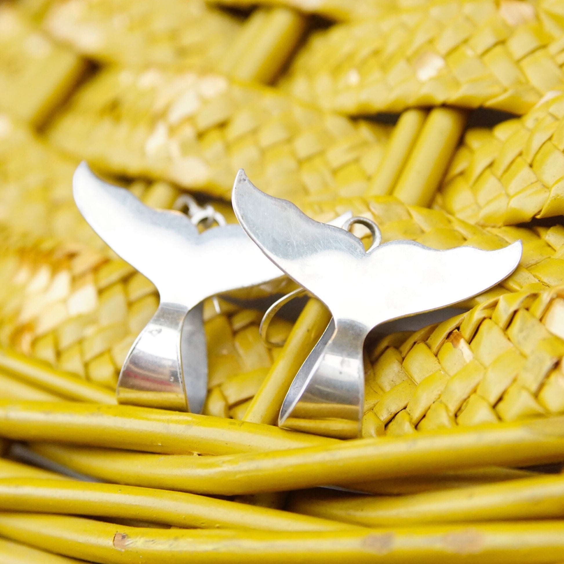 Silver whale tail earrings on woven yellow background