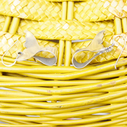 Yellow woven wicker basket texture background with pair of silver whale or dolphin tail dangle earrings