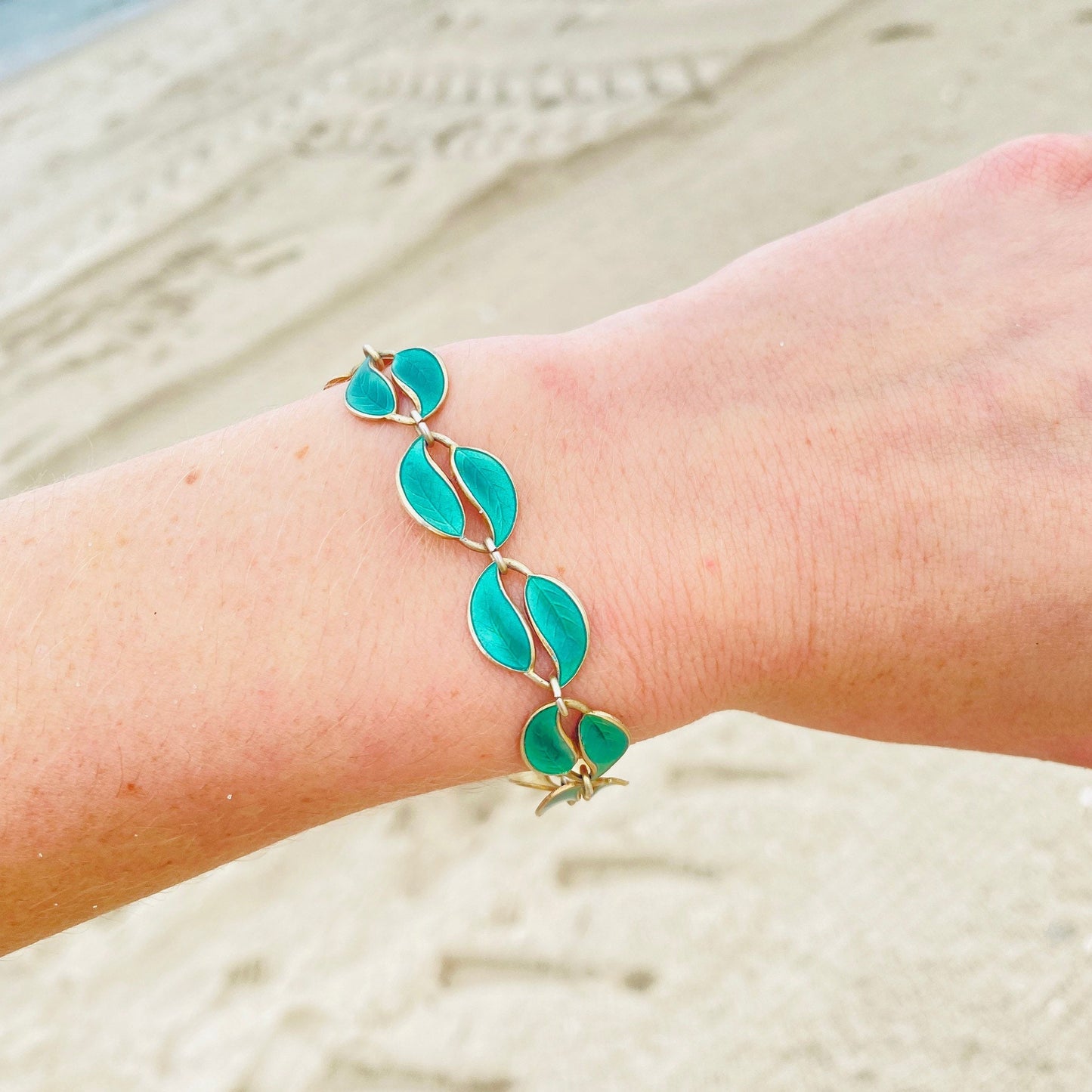 Vintage David Anderson Norway sterling silver guilloche enamel leaf bracelet with double leaf links and gold tone accents on a wrist, resting on sand at the beach