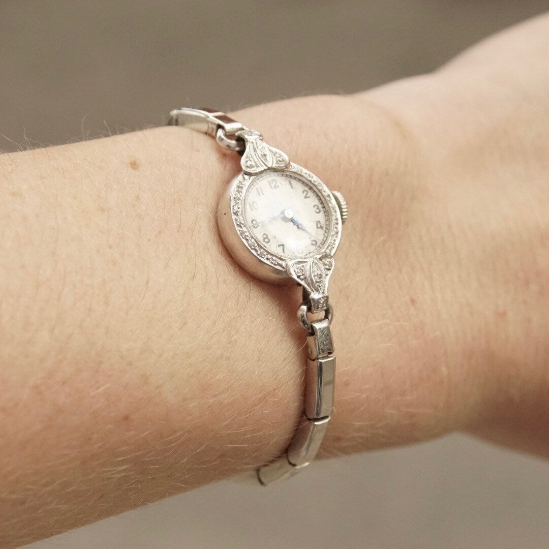 Vintage platinum ladies wrist watch with diamond encrusted case and stretch band, featuring hand winding analog movement, measuring 5 1/2 inches long, in working condition.