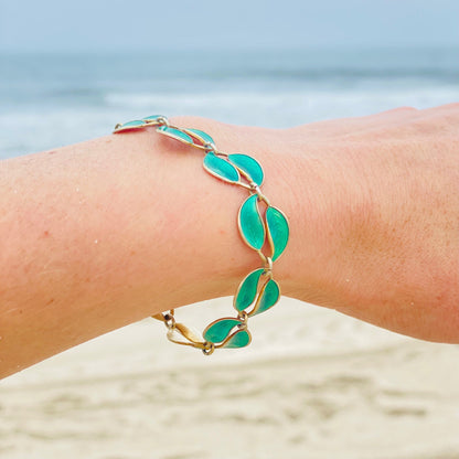 Vintage David Anderson Norway sterling silver and guilloche enamel leaf bracelet on a wrist at the beach, featuring double leaf links in green enamel and gold tone silver.