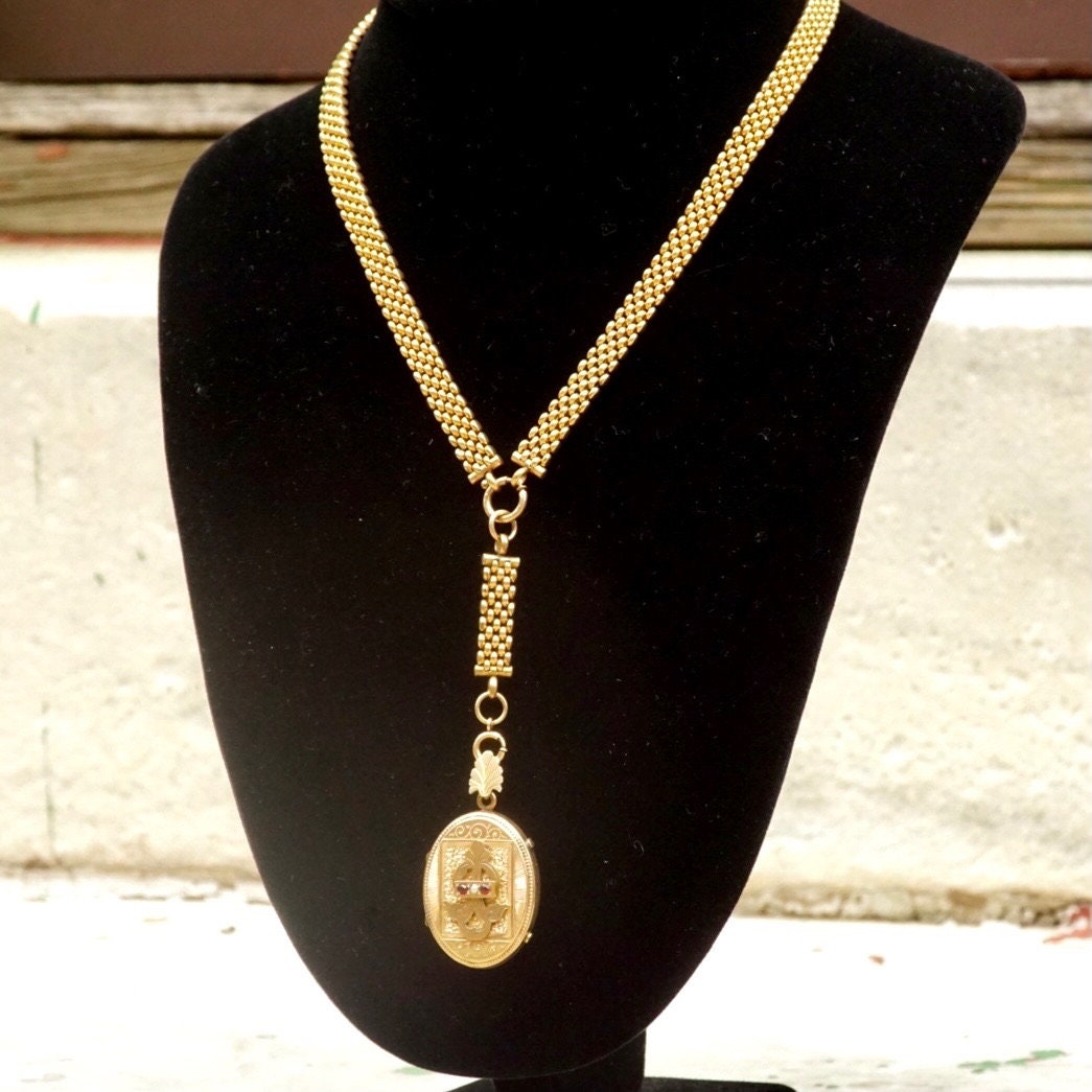 Victorian mourning locket necklace with gold-filled pendant, etched cameo design, and thick gold chain on black velvet display stand