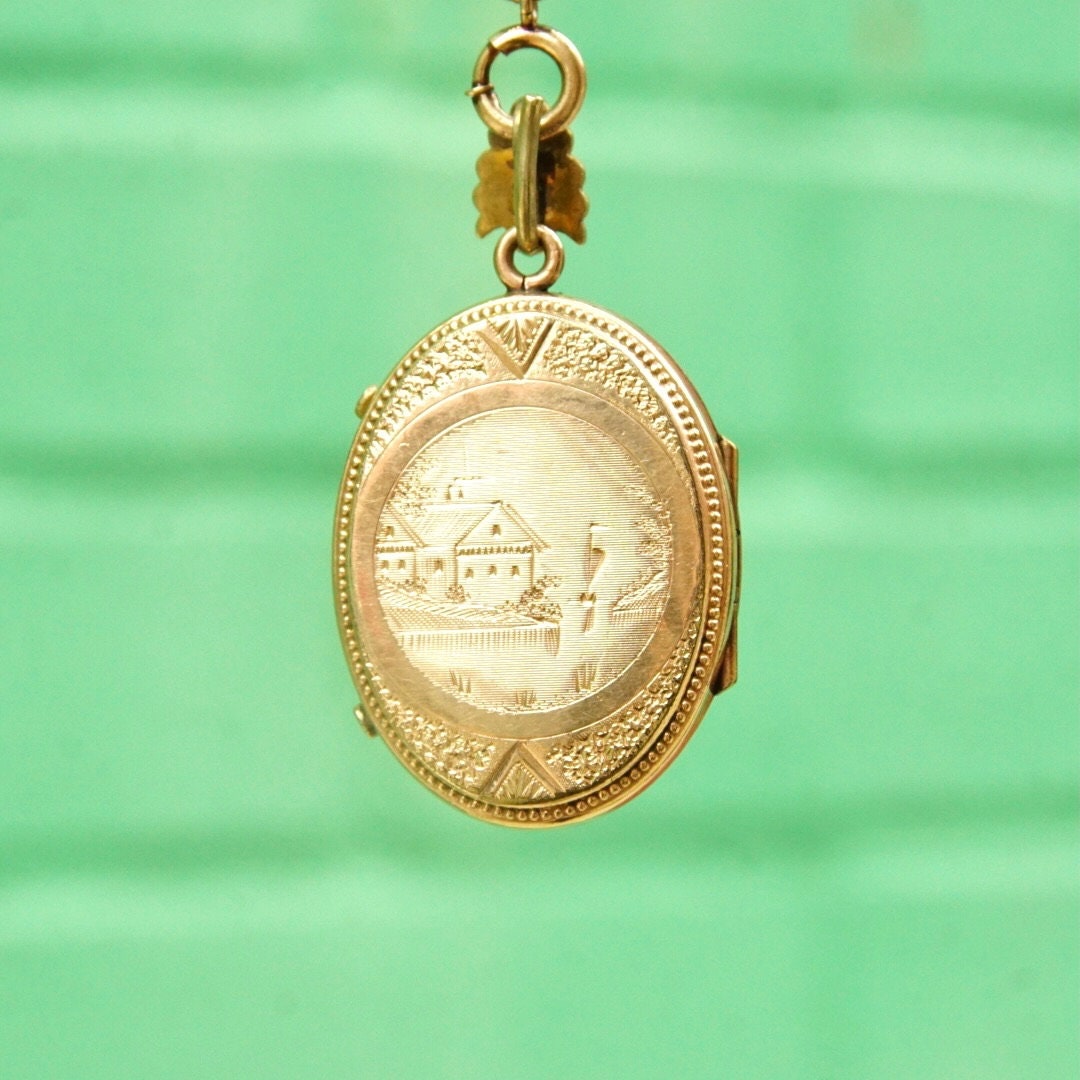 Antique Victorian gold-filled locket pendant featuring an etched cameo design, accented with a garnet or diamond, suspended from a thick gold chain, representing a piece of mourning jewelry from the era.