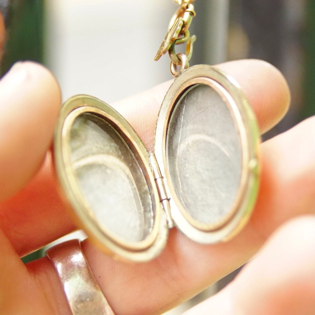 Victorian gold-filled locket pendant necklace with etched cameo design and garnet or diamond stone, held in hand to show detail of thick gold chain and ornate locket.