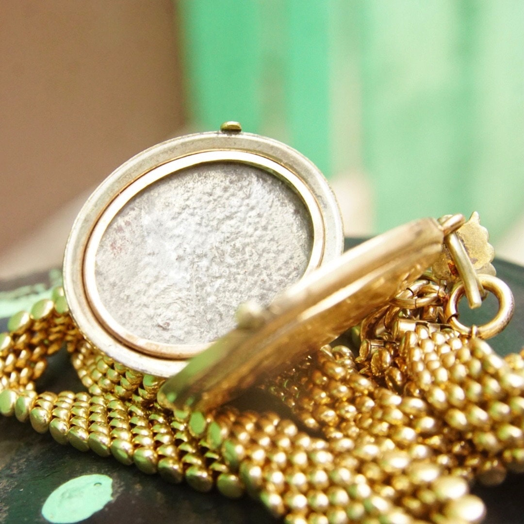 Victorian gold-filled locket pendant necklace with garnet or diamond, featuring an etched cameo design, on a thick gold chain, representing mourning jewelry from the Victorian era.