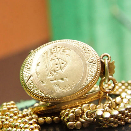 Alt text: Antique gold Victorian locket pendant with etched cameo design on thick gold chain, featuring garnet or diamond accent, used as mourning jewelry in the 19th century