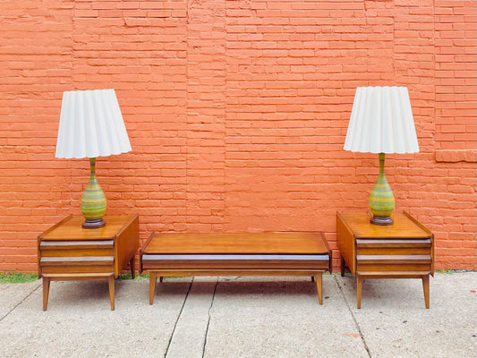 Vintage Mid Century Modern LANE First Edition coffee and end table set with walnut and pecan finish, style number 1062 01, flanked by two table lamps against an orange brick wall.