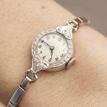 Vintage platinum and diamond ladies wrist watch with hand winding mechanism, analog dial, diamond encrusted case, and stretch band, measuring 5 1/2 inches long, in working condition.