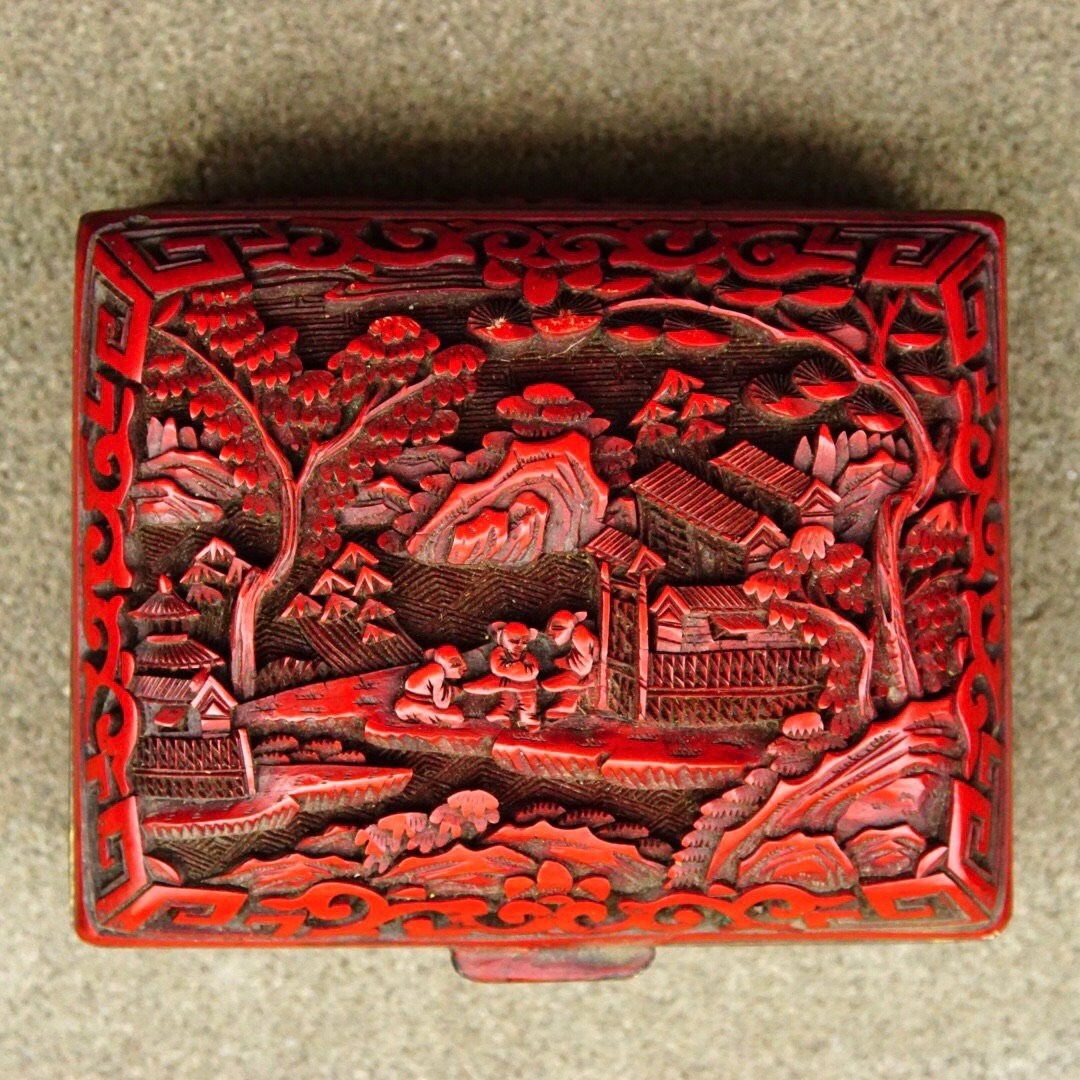 Antique Chinese carved cinnabar enamel hinged box featuring intricate landscape carving with flora, fauna and figural motifs on the lid. Rectangular shaped box measures 4 inches wide, 3.5 inches deep and 2 inches tall.