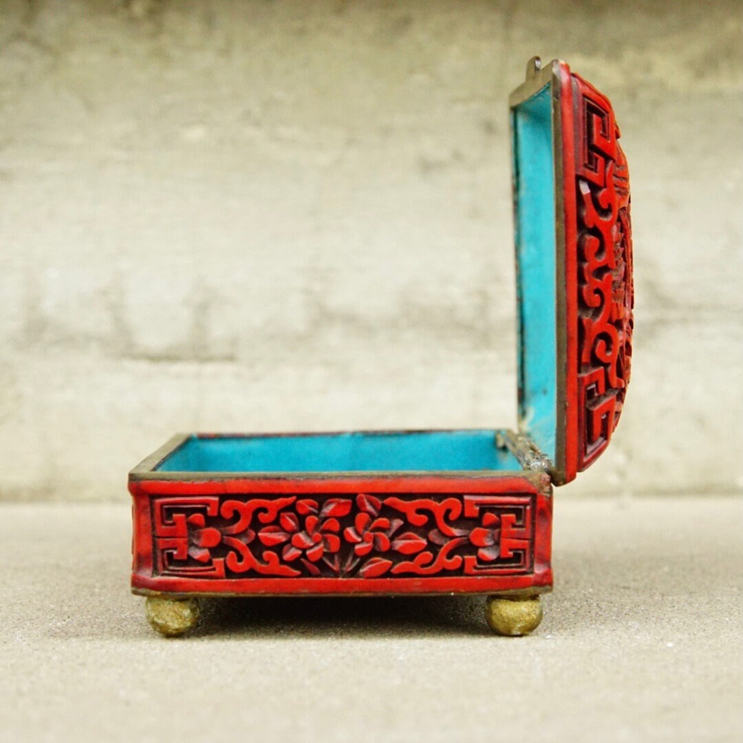 Antique Chinese carved cinnabar enamel box with intricately carved floral and fauna motifs on the sides and lid, featuring a turquoise interior. The ornate red and turquoise lacquered wooden box sits open, measuring approximately 4 inches wide, 3.5 inches deep and 2 inches tall.