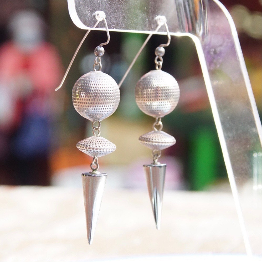 Vintage modernist silver ball and hematite spike dangle earrings, reflecting light, hanging from silver earring hooks against blurred background