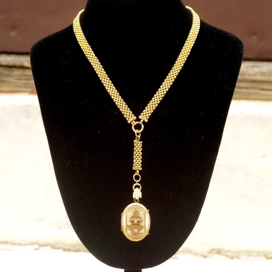 Antique Victorian gold-filled mourning locket pendant necklace featuring an etched cameo design, adorned with a garnet or diamond, suspended from a thick gold chain, showcasing the intricacy and sentiment of traditional mourning jewelry from the era.