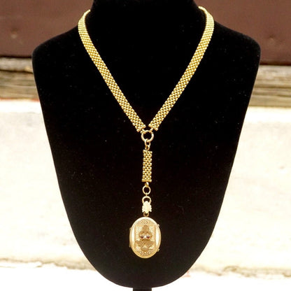 Antique Victorian gold-filled mourning locket pendant necklace featuring an etched cameo design, adorned with a garnet or diamond, suspended from a thick gold chain, showcasing the intricacy and sentiment of traditional mourning jewelry from the era.