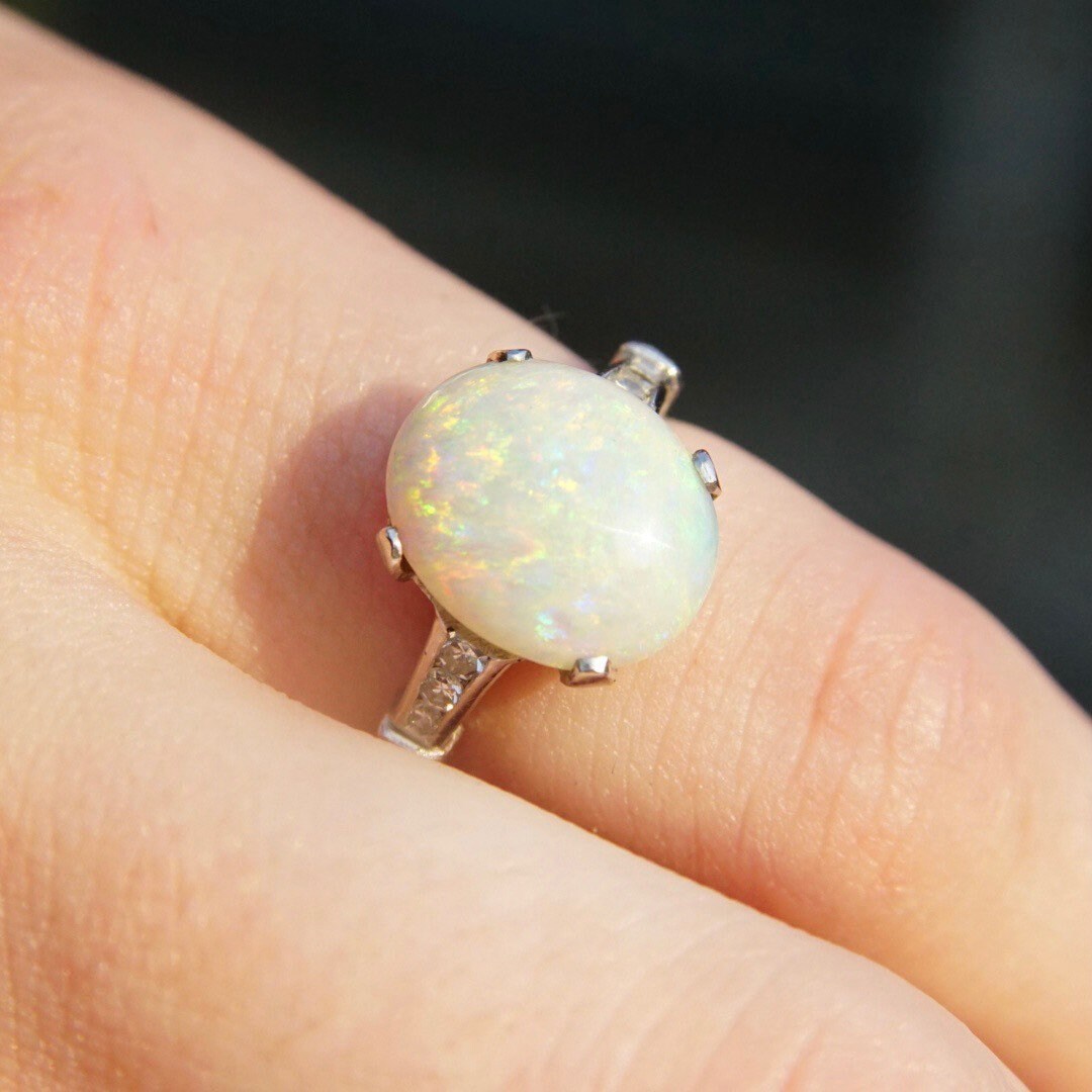 Vintage 14K white gold opal ring with iridescent white opal stone and accent diamonds, showcasing a petite cocktail design in a cathedral setting, sized at 5 1/2 US, displayed on a person's finger.