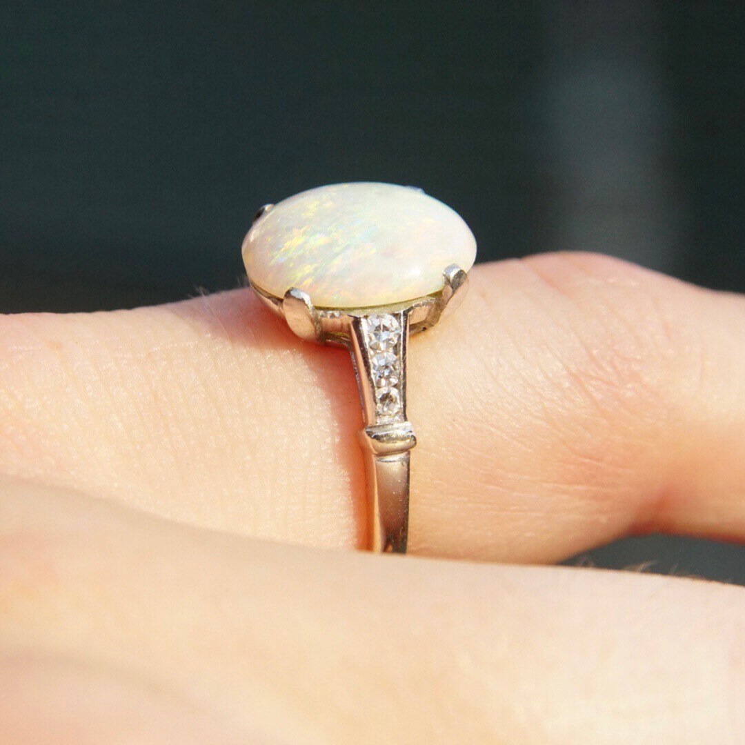 Vintage 14K white gold opal ring with iridescent white opal stone and accent diamonds, showcasing a petite cocktail design in a cathedral setting, sized at 5 1/2 US, held on a person's finger.