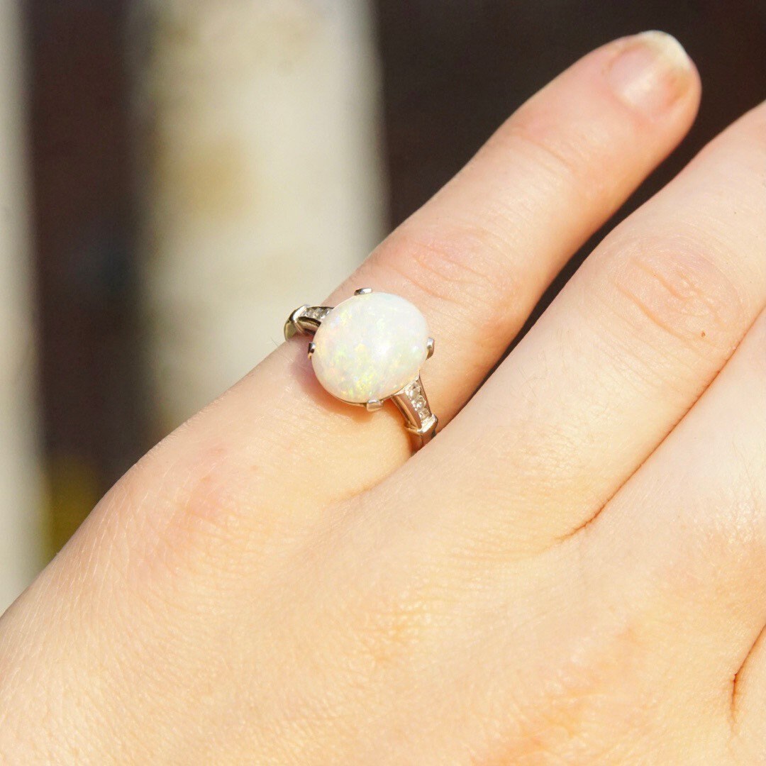 Vintage 14K white gold opal ring with iridescent white opal stone and accent diamonds in a petite cathedral setting, shown on a person's hand, size 5 1/2 US.